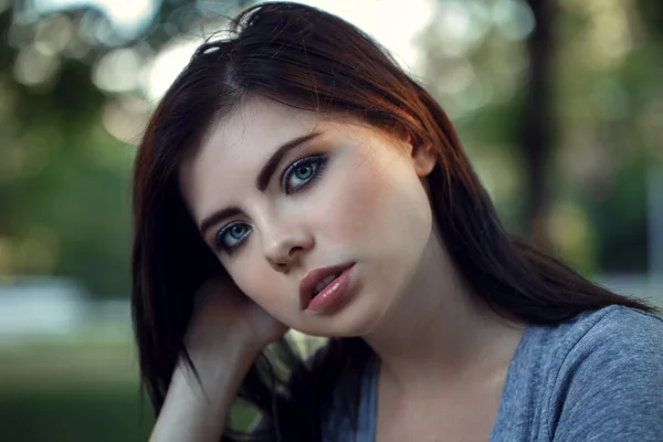 Closeup portrait of beautiful young sexy Caucasian woman with red black hair, blue eyes, looking in camera, sitting outdoors on sunset, summer evening, natural beauty youth look