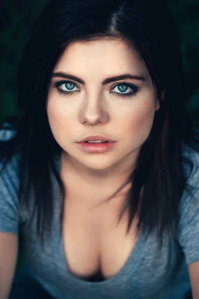 Closeup portrait of beautiful young sexy Caucasian woman with black hair, blue eyes, looking in camera, sitting outdoors, toned with filters, natural beauty youth look, top above view