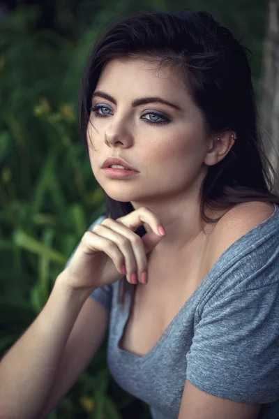 Closeup portrait of beautiful sexy young Caucasian woman with black hair, blue eyes, looking away, sitting outdoors, in grey open tshirt, natural beauty youth look