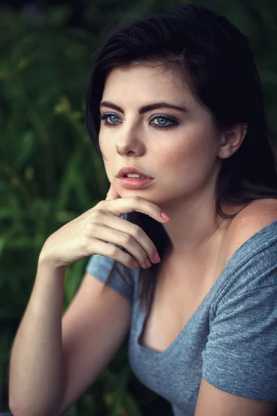 Closeup portrait of beautiful sexy young Caucasian woman with black hair, blue eyes, looking away, sitting outdoors, in grey open tshirt, natural beauty youth look