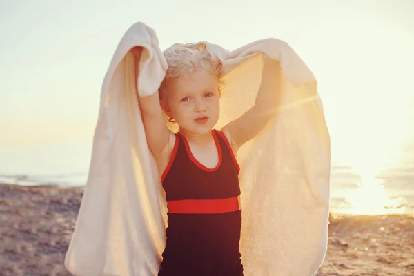 Portrait of cute adorable happy smiling toddler little girl with towel on beach making poses faces having fun, emotional face expression, lifestyle sunset summer mood, toned