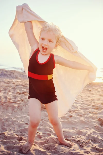 Portrait of cute adorable happy smiling toddler little girl with towel on beach making poses faces having fun, emotional face expression, lifestyle sunset summer mood, toned