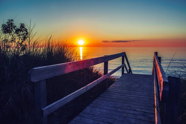 Beautiful evening sunset landscape at Canadian Ontario lake Huron in Pinery Park, orange blue red sky sun. Amazing summer sunset view on the beach. Dunes, grass, wooden stair leading to water