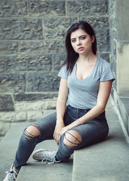 Portrait of white Caucasian beautiful young brunette girl teenager with blue green eyes in ripped jeans, t-shirt, keds  looking in camera. Toned with filters, lifestyle concept.