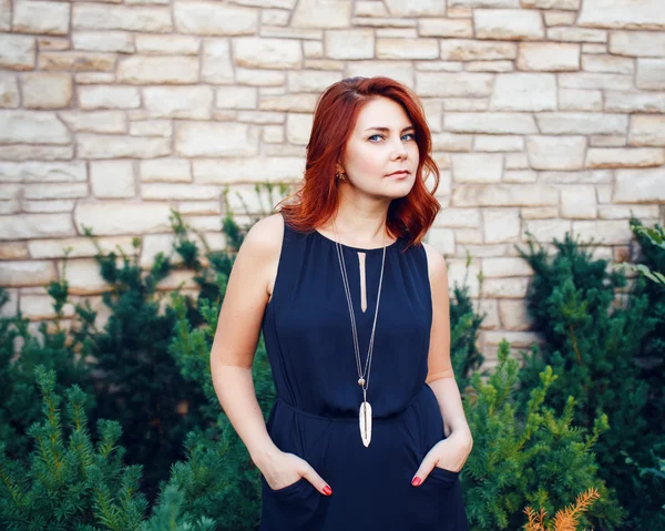 Closeup portrait of sexy middle aged white caucasian woman with waved curly red hair in black dress looking in camera outside in park, beauty fashion lifestyle concept