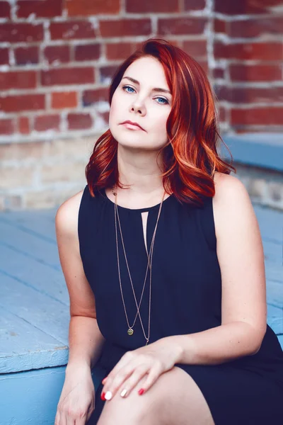 Closeup portrait of smiling middle aged white caucasian woman with waved curly red hair in black dress looking in camera sitting outside, beauty fashion lifestyle concept