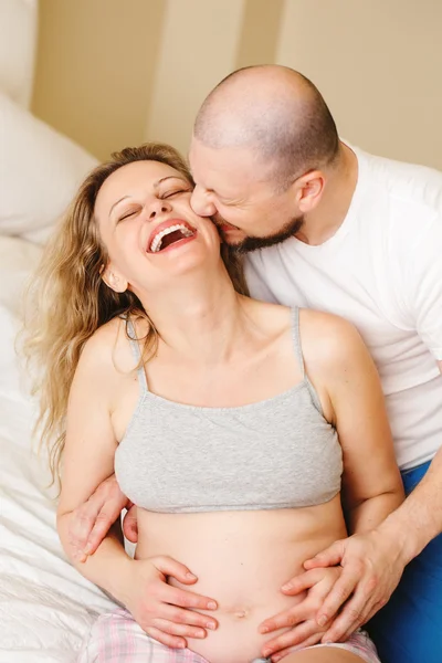 Portrait of smiling laughing white Caucasian young middle age couple, pregnant woman with husband in room on couch hugging cuddling, lifestyle maternity concept