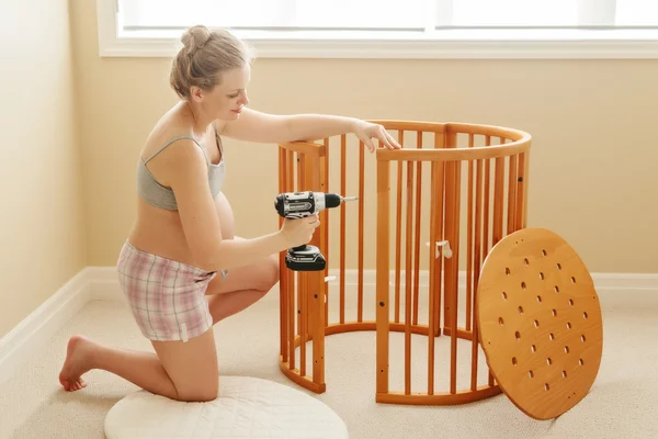 Portrait of young white Caucasian happy woman assembling wooden baby crib in nursery at home, lifestyle single mother busy woman concept
