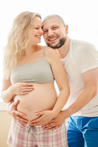 Portrait of smiling laughing white Caucasian young middle age couple, pregnant woman with husband in room hugging cuddling, lifestyle maternity concept