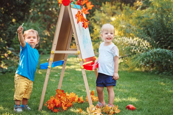 Group of two white Caucasian toddler children kids boy and girl standing outside in summer autumn park by drawing easel with markers, playing studying learning, back to school