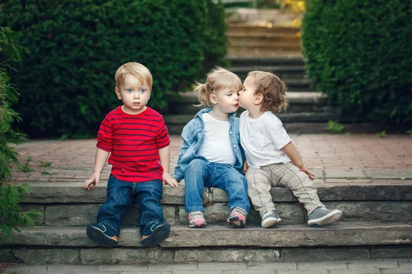 Group of three cute funny adorable white Caucasian children toddlers boys girl sitting together kissing each other, love friendship childhood concept, best friends forever
