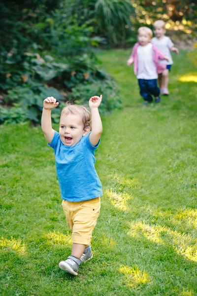 Group portrait of three white Caucasian blond adorable cute kids playing running in park garden outside on bright summer spring day enjoying happy childhood life, having fun.