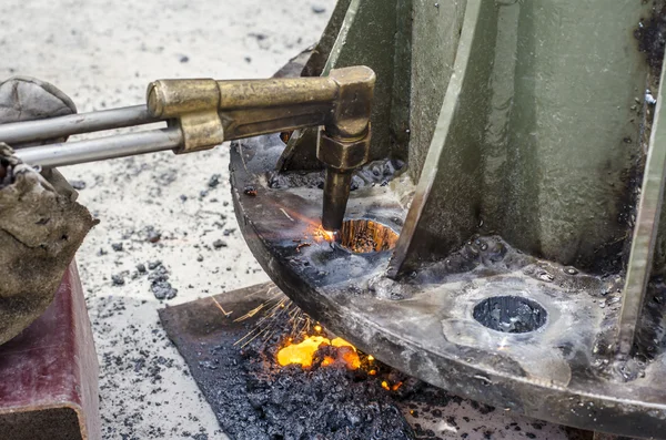 Black smith making hole on steel plate by using gas and fire