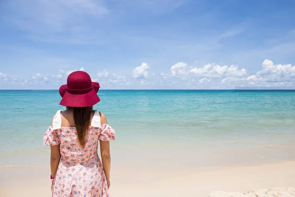 Woman wear dress and beach hat stand on beach enjoying looking at the ocean in summer holidays