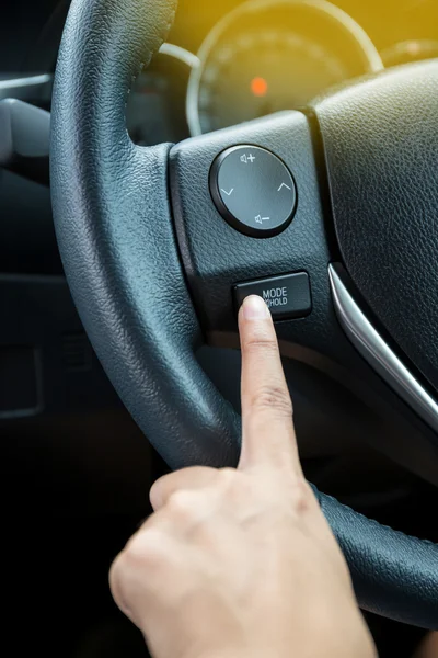 A woman hand pushes the mode hold control button on a steering wheel.