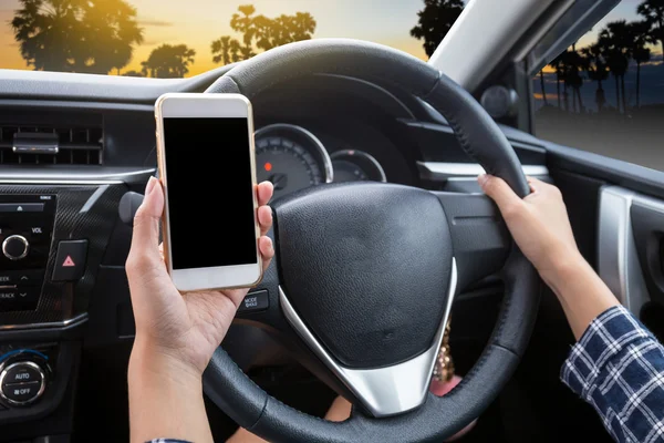 Young woman driver using touch screen smartphone and hand holding steering wheel in a car with palm tree at sunset or twilight background