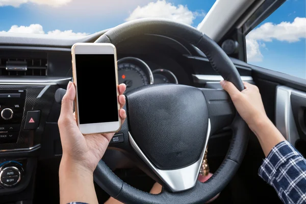 Young woman driver using touch screen smartphone and hand holding steering wheel in a car with blue sky and cloud background