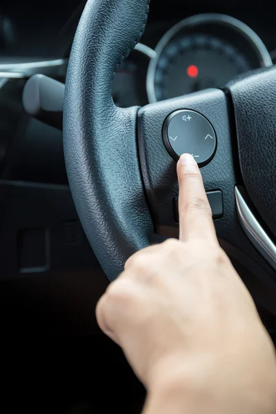 A woman hand pushes the volume control button on a steering wheel.