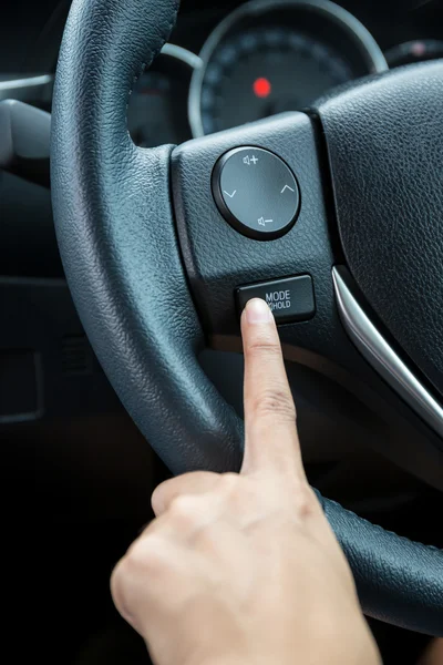 A woman hand pushes the mode hold control button on a steering wheel.