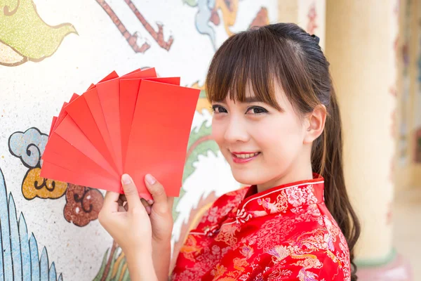 Happy chinese new year,Cute smiling Asian woman dress traditional cheongsam and qipao holding red envelopes ang pow or red packet monetary gift card on chinese pattern traditional background