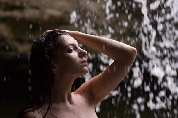 Outdoor photo of sexy beautiful woman with brunett hair in bikini relaxing under a waterfall