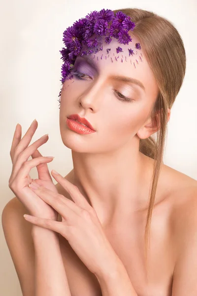Portrait of young beautiful fresh girl with stylish make-up and purple flowers around her face and hair.