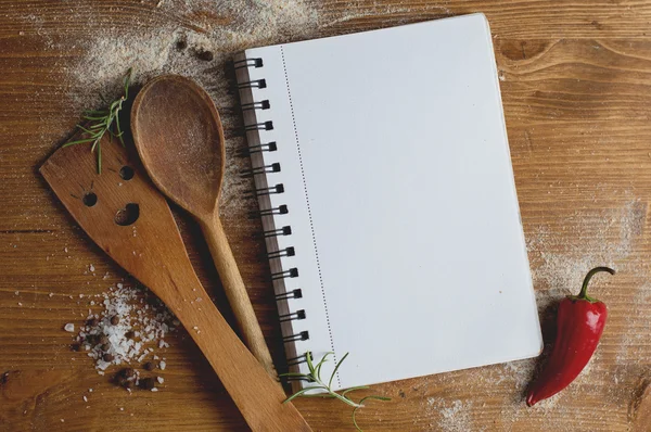 Open recipe book with wooden spoon, spatula and spices