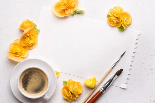 Blank notepad, flowers, brushes and cup of coffee over white woo