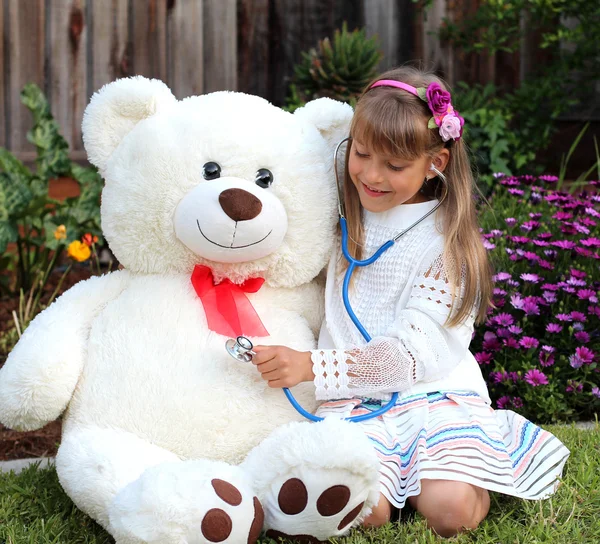 Smiling girl plays the doctor with huge toy white bear