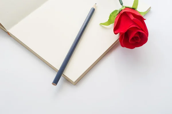Red rose on a notebook and pencil