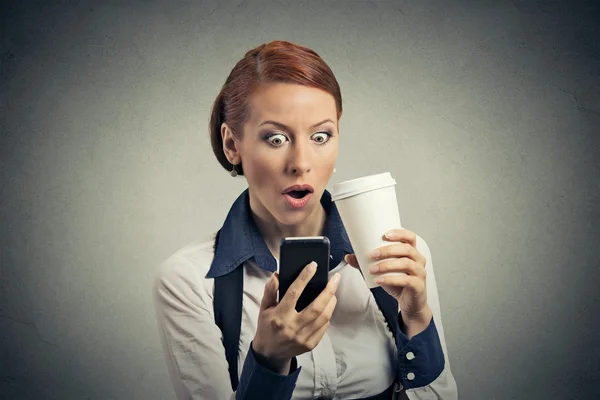 Surprised business woman reading news on smart phone drinking soda coffee