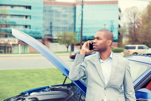 Stressed man having trouble with broken car opening hood calling for help on cell phone