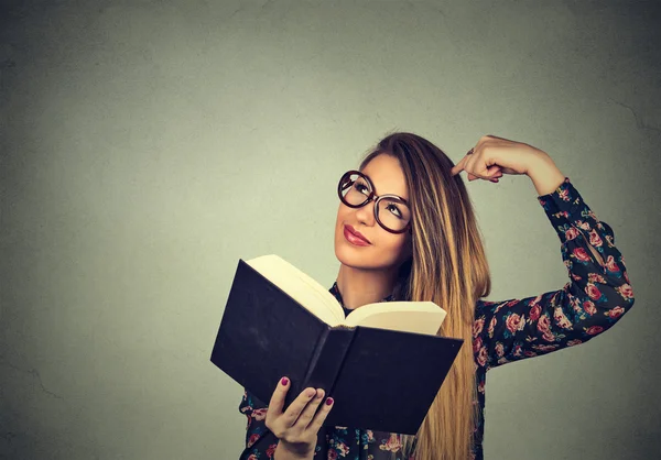 Woman with glasses, holding, reading book, scratching head, looking up confused