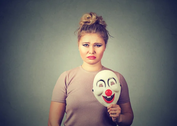 Upset woman with sad expression holding clown mask expressing happiness