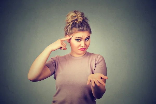 Angry mad young woman gesturing with her finger against temple asking are you crazy?