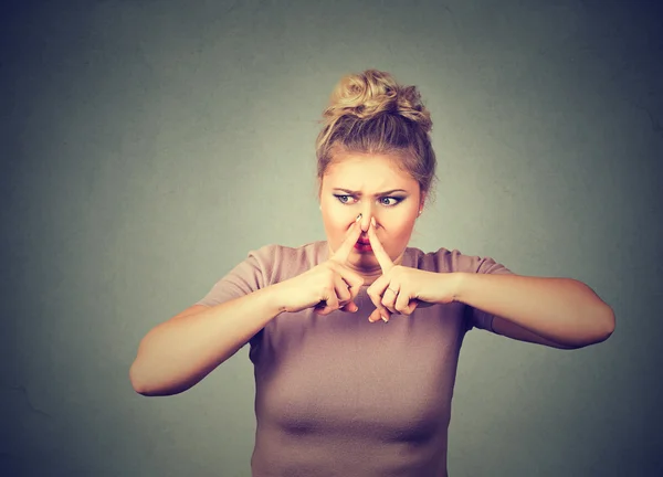 Woman pinches nose with fingers hands looks with disgust something stinks bad smell