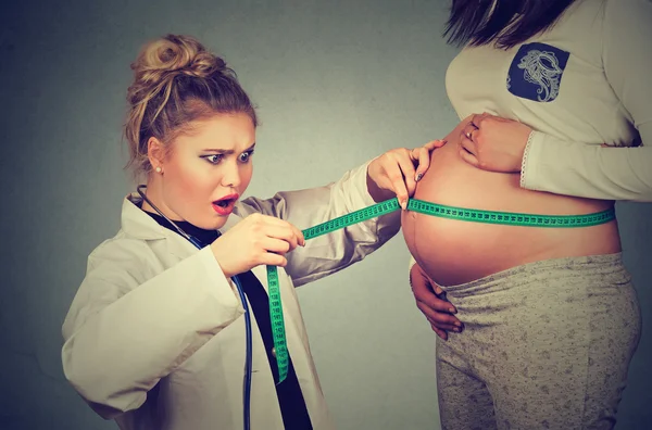Pregnant woman exposing belly while a shocked gynecologist doctor uses measuring tape to follow growth of baby