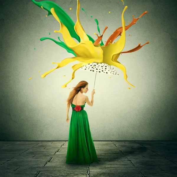 Beautiful woman in green dress with umbrella as shelter against colorful drops splashes of paint falling down