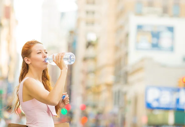 Thirsty woman. Woman drinking water from plastic bottle in a city on hot summer day