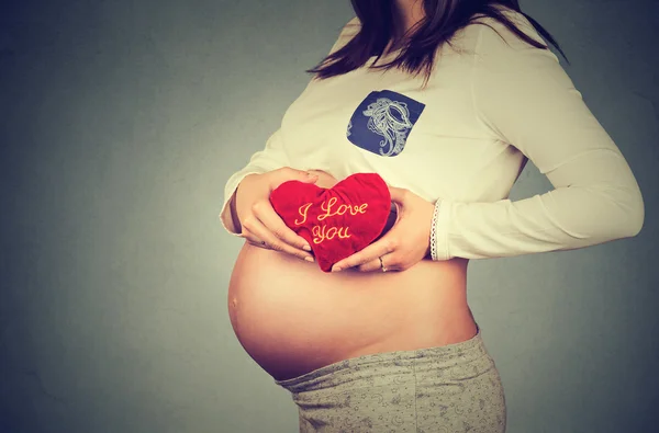 Pregnant woman\'s belly with heart shaped red pillow. Human pregnancy concept