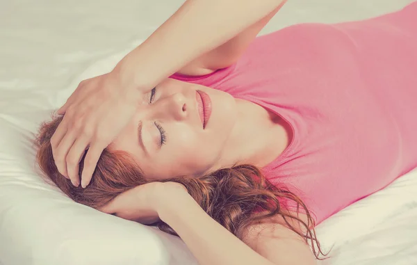 Sad woman lying in bed with her arms on head and eyes closed having headache