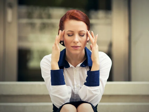 Stressed sad woman sitting outdoors having headache. City urban life style stress