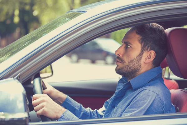 Scared funny looking young man driver in the car. Inexperienced anxious motorist