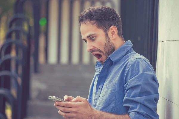 Anxious man looking at phone seeing bad message or photos with disgusting emotion on face