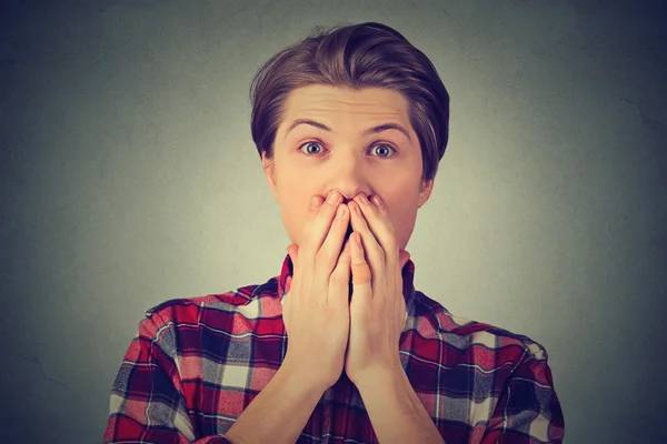 Portrait of a shocked young man covering his mouth with hand