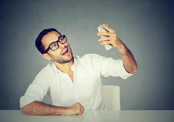 Young funny looking man taking pictures of him self with smart phone