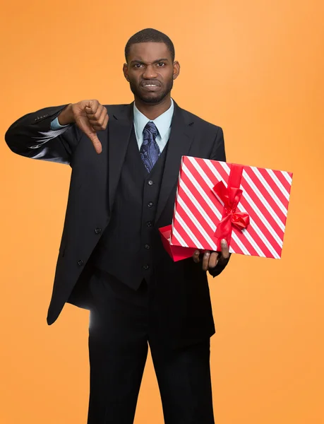 Upset man holding gift box displeased, showing thumbs down