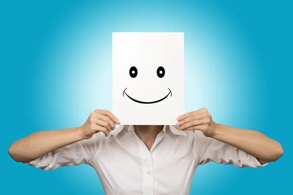 Woman covering face with smiling paper mask