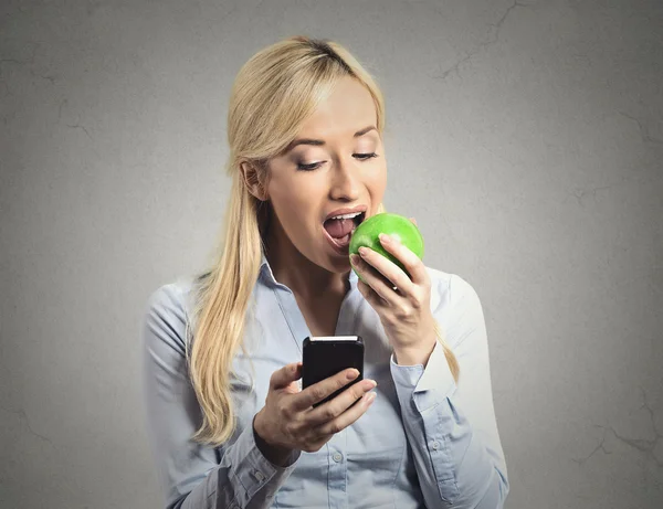 Business woman reading news on smartphone eating green apple
