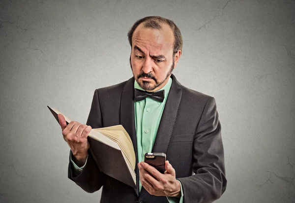 Skeptical man reading news on smartphone, holding book